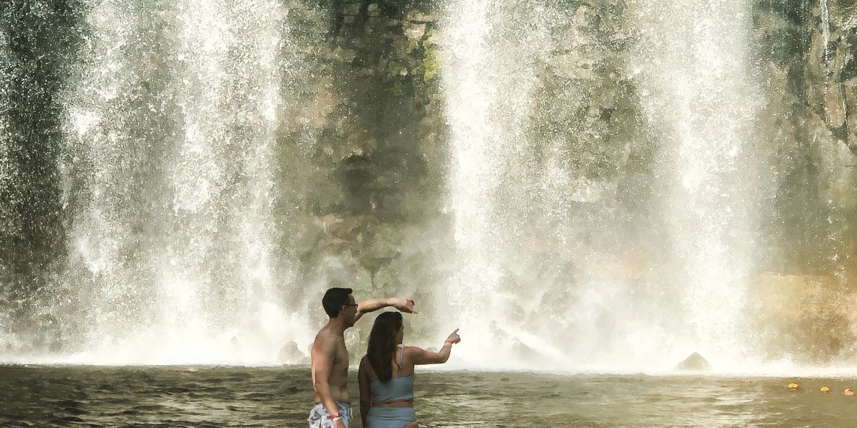 Pareja de Viajeros tomando un baño frente a una catarata en Costa Rica