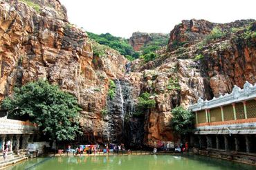 Waterfall cascading down rocky cliffs into a green pond at a temple site.