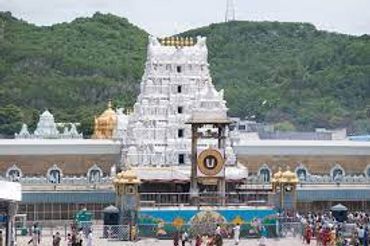 A grand Hindu temple with a white gopuram against green hills.