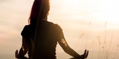 Silhouette of a person meditating at sunrise or sunset outdoors.