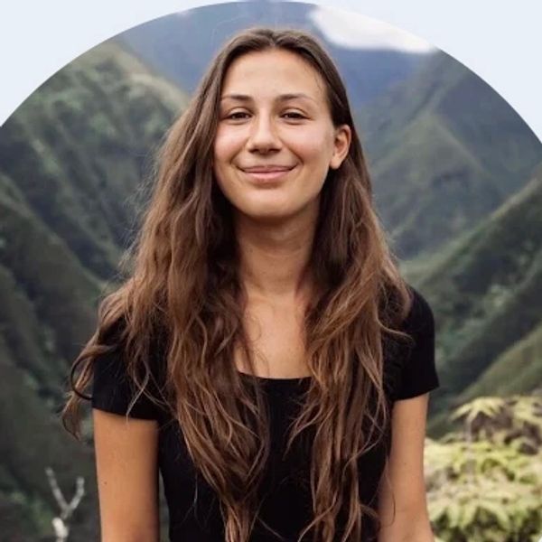 Young woman smiling outdoors with mountain backdrop.