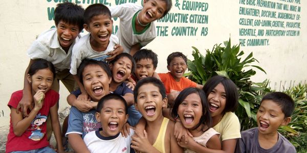 A joyful group of children laughing together outdoors by a wall with motivational text.