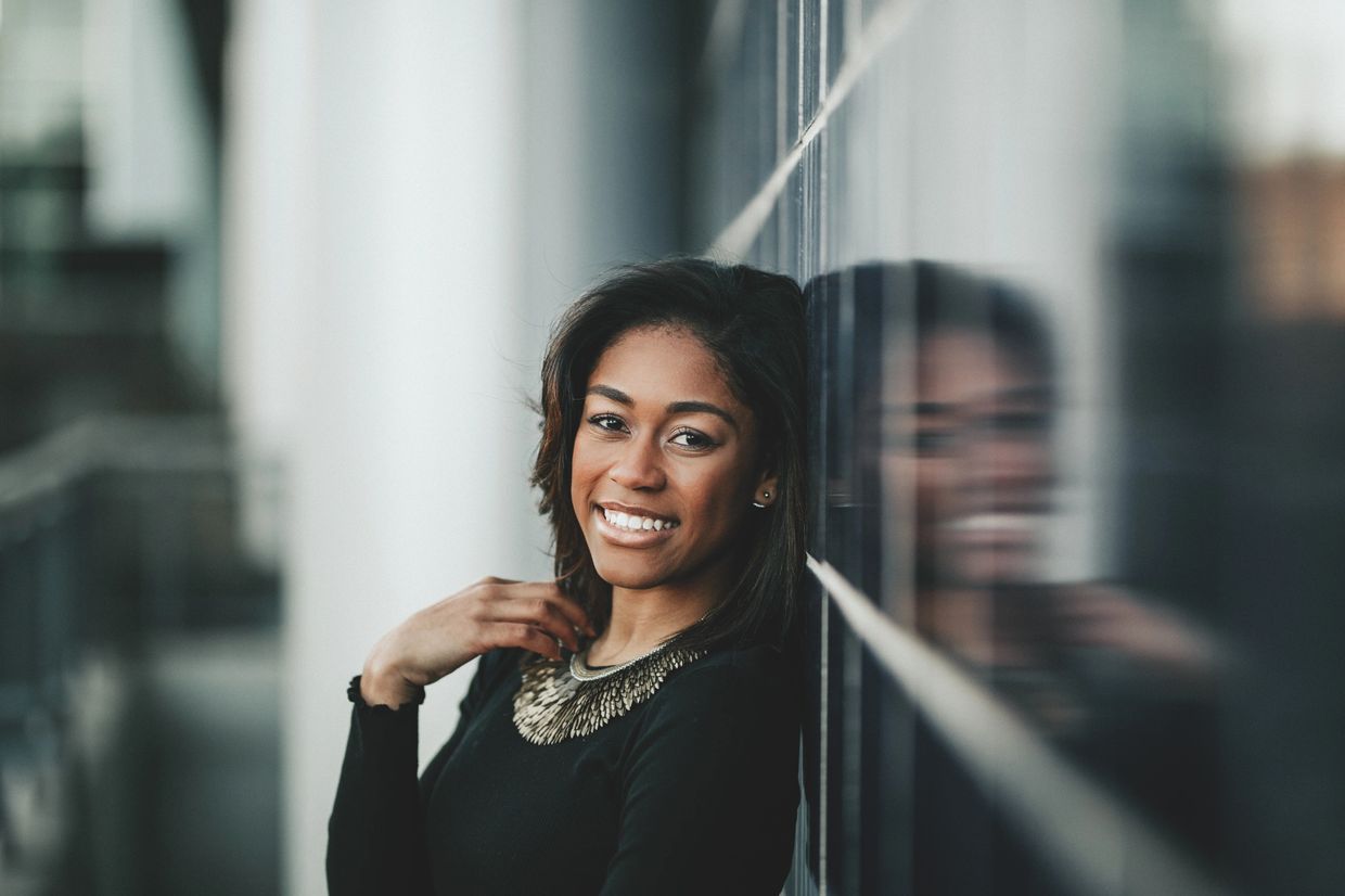 Smiling woman leaning against a reflective glass wall.
