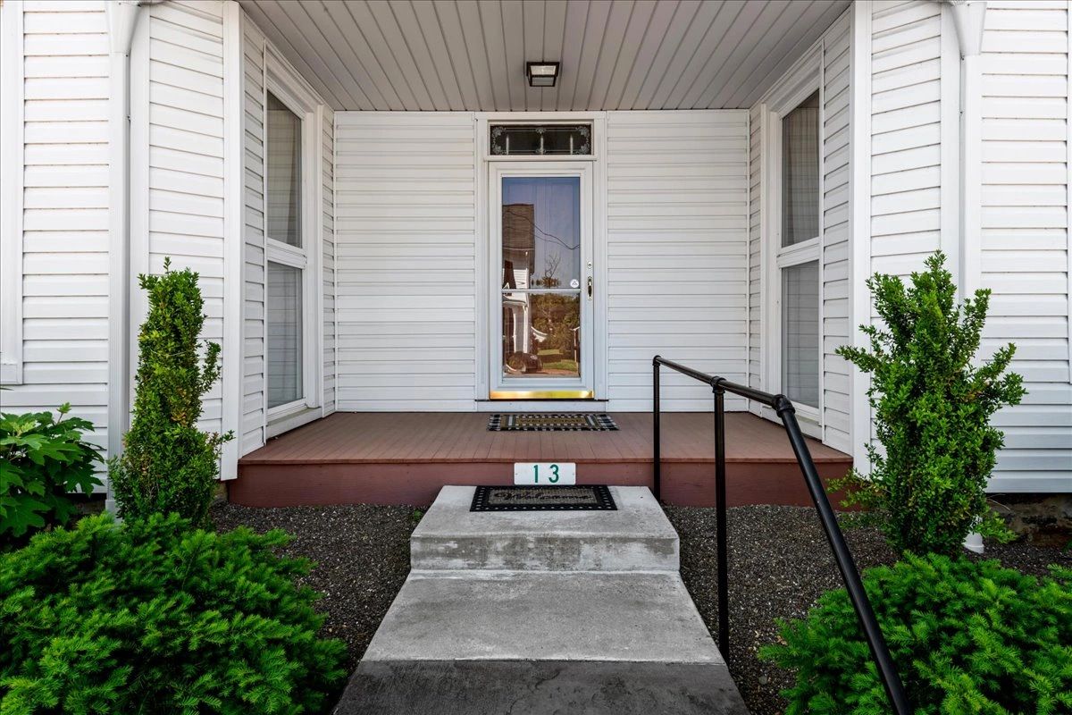 Entrance of a white house with concrete steps and greenery.