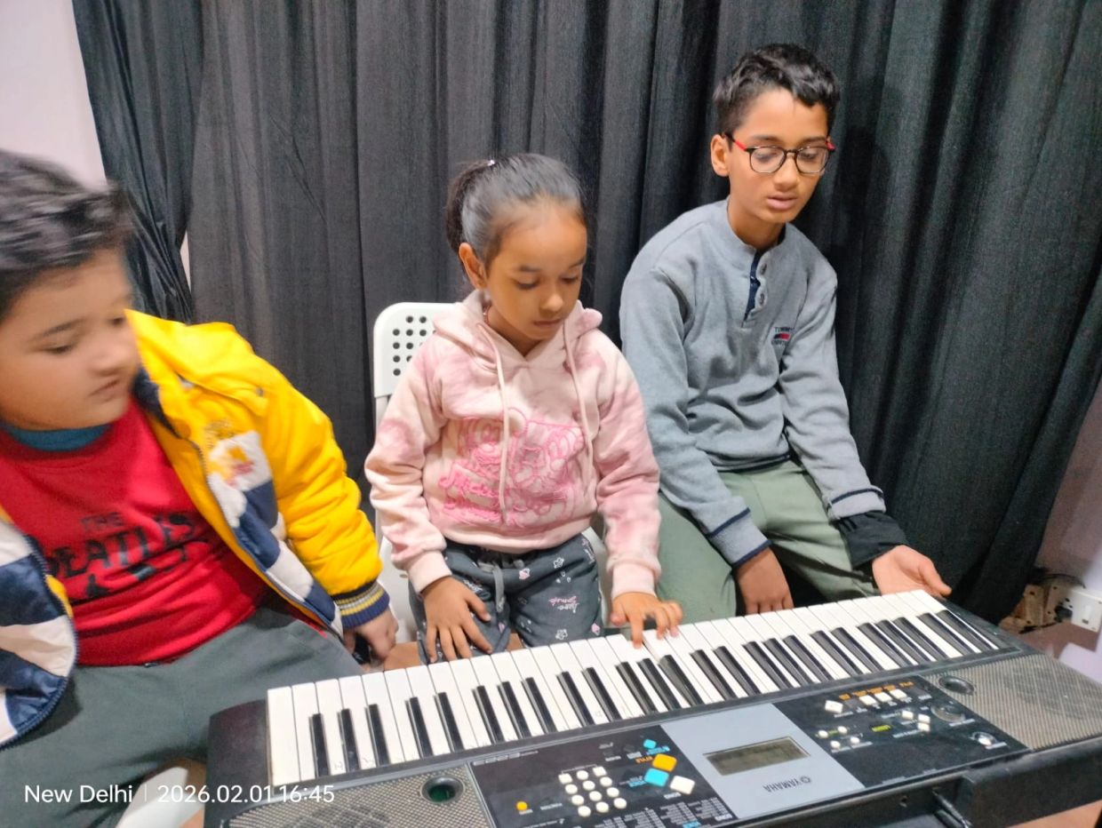 Three children sitting by a keyboard piano, with two focused on playing.