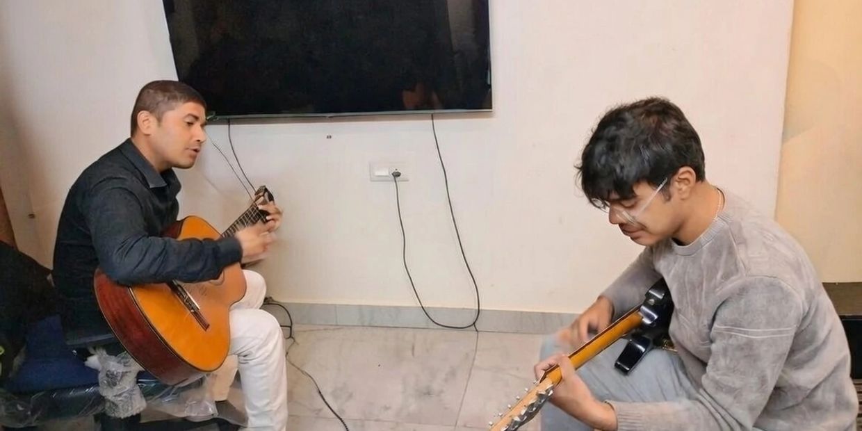 Two men playing guitars together indoors.