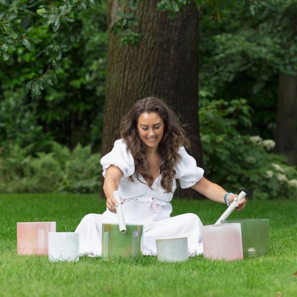 Woman playing crystal singing bowls outdoors.