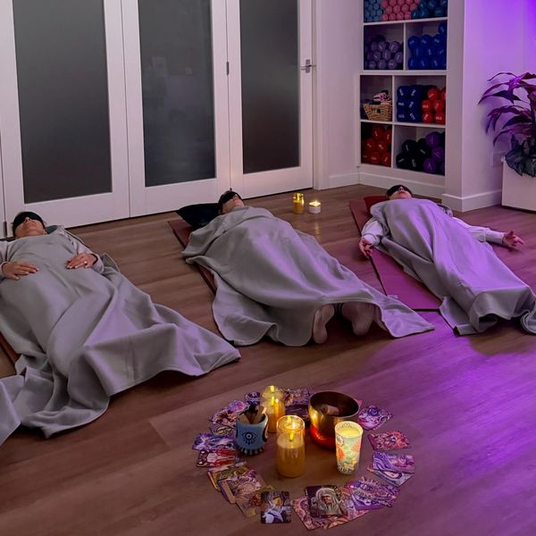 Three people relaxing on mats with blankets and candles around.