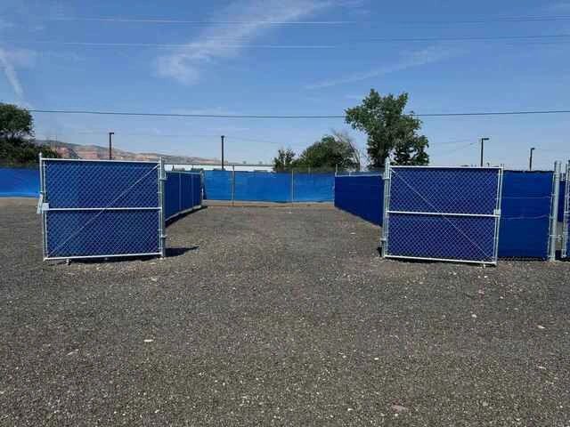 An outdoor area with blue mesh-covered chain-link fences on gravel ground. Contractor yard. 