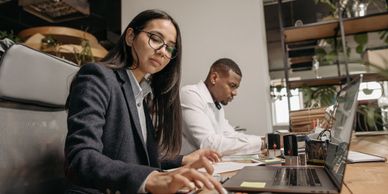 Two professionals working at a desk with laptops.