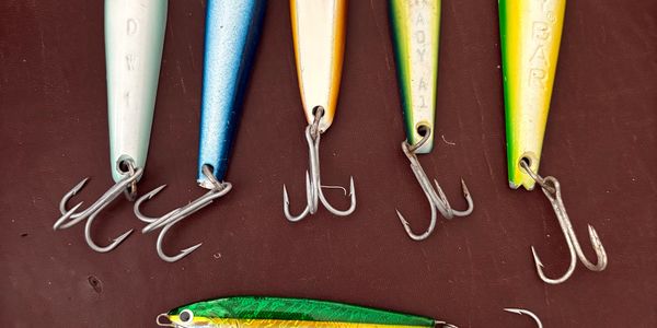 Close-up of colorful fishing lures with sharp treble hooks on a brown surface.