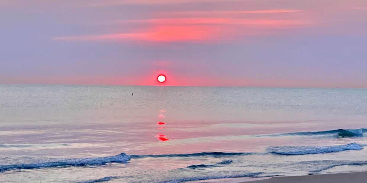 A serene sunset over calm ocean waves with pink and purple sky hues.