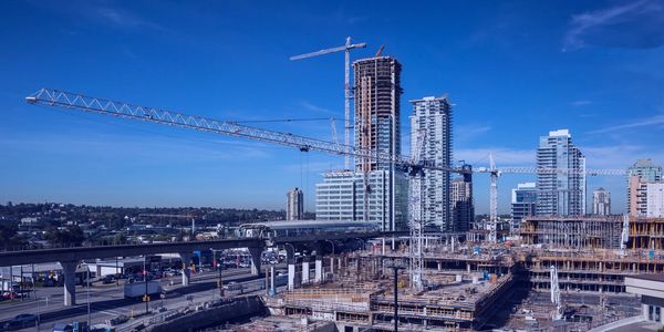 Urban construction site with cranes and high-rise buildings under a clear blue sky.