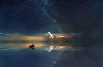Sailboat on calm water under starry night sky with Milky Way.