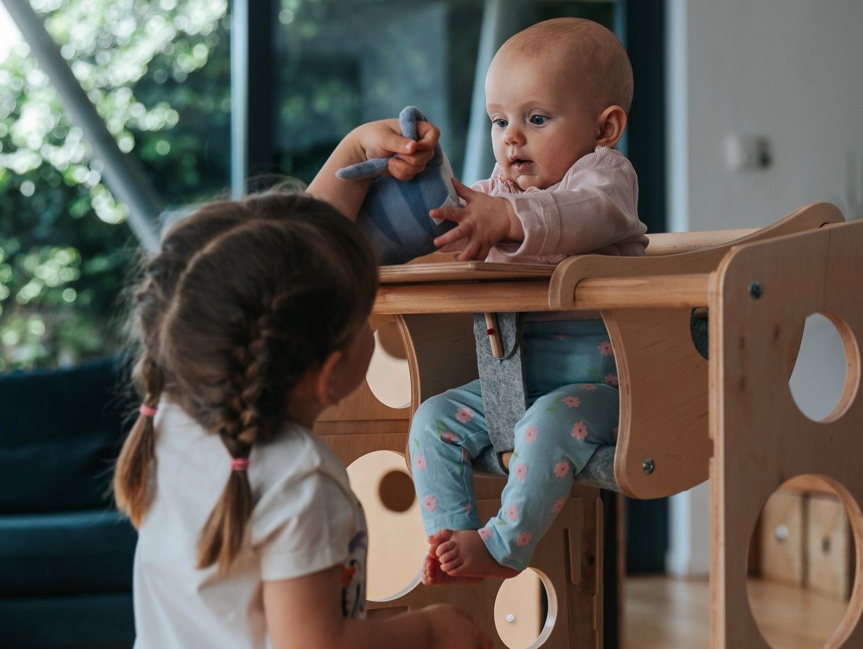Anastasia hilft ihrer Schwester, das Spielzeug zu erreichen. ZOe sitzt auf dem Schaukelstuhl von Lee