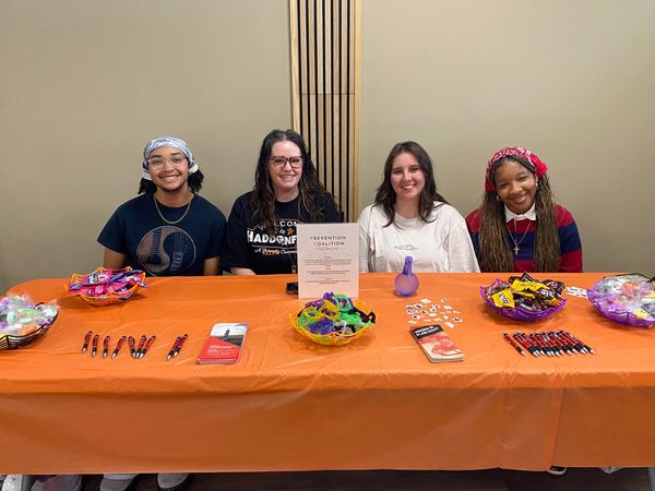 Four people smiling behind an orange table with informational items and candy.