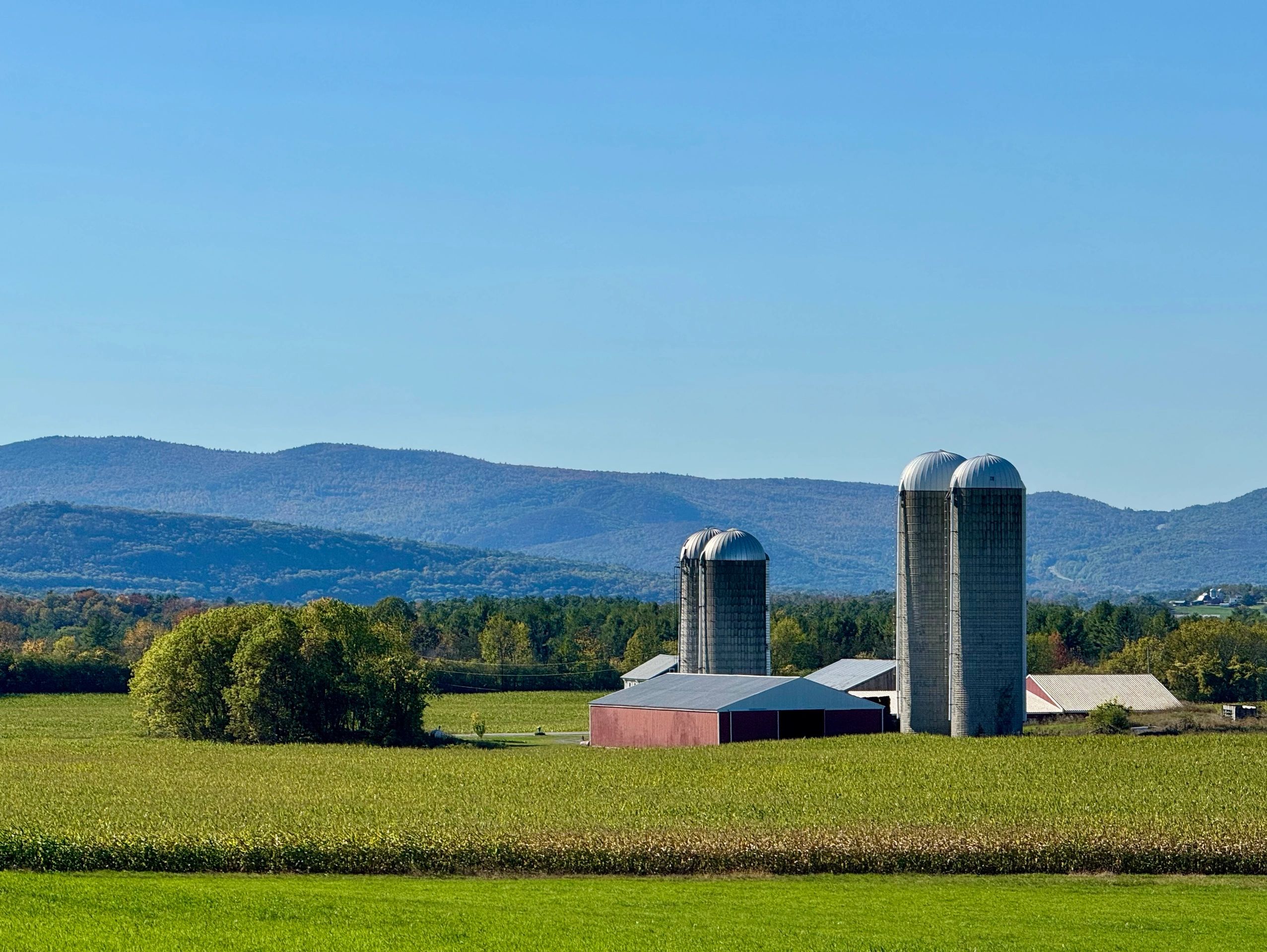 Farm silos and barns with mountains in the background under a clear sky.