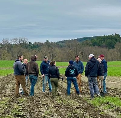 Group of people standing in a muddy field having a discussion on a cloudy day.