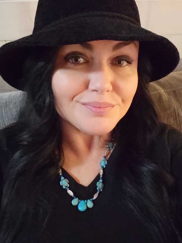 Woman with dark hair wearing a black hat and turquoise necklace.