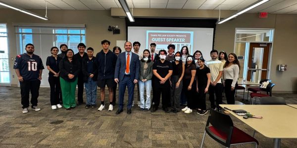 Group photo of diverse students and a guest speaker in a conference room.