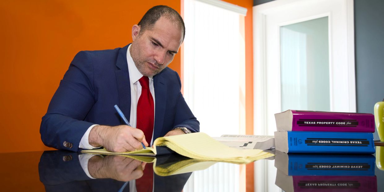 A man in a suit writing notes beside legal books on a reflective table.