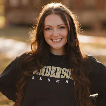 Smiling young woman wearing an Anderson Alumni sweatshirt outdoors.