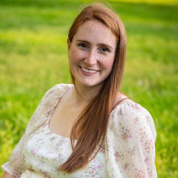 Smiling woman with long red hair in floral dress outdoors.