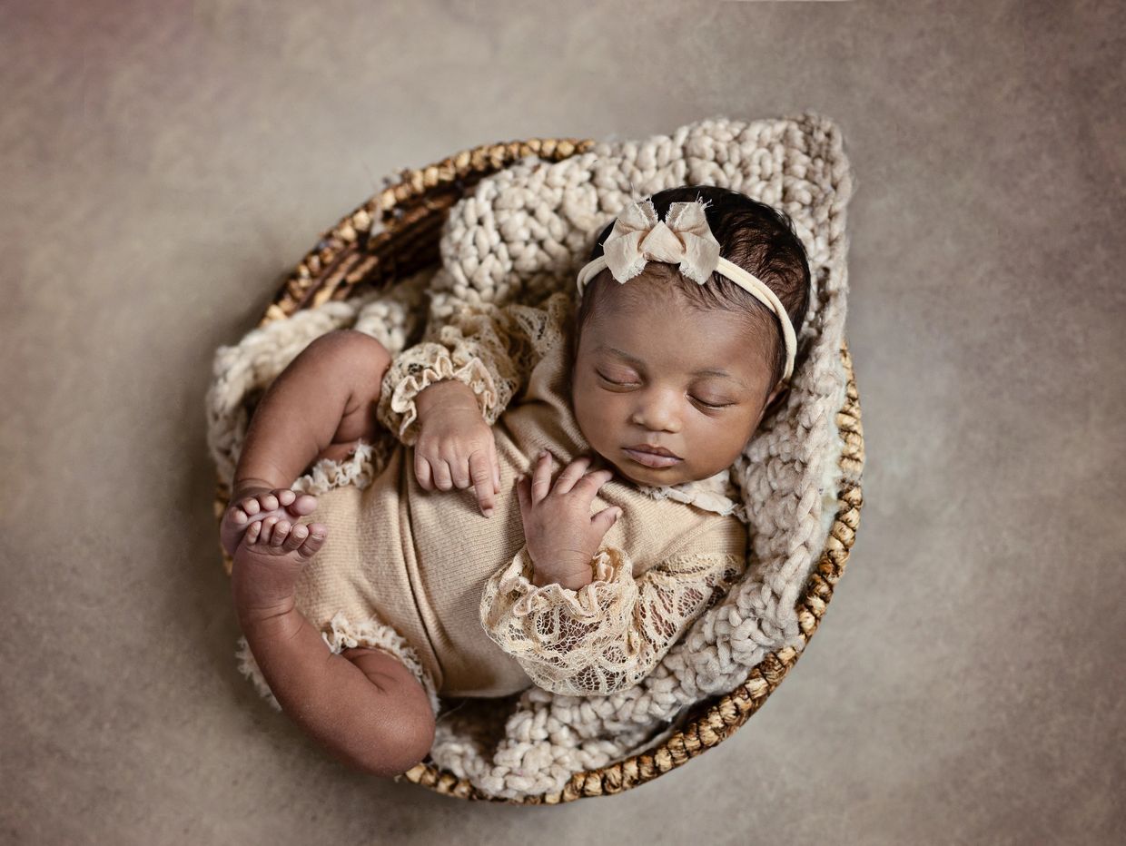 A sweet baby girl sleeps in a round basket with her feet touching each other.