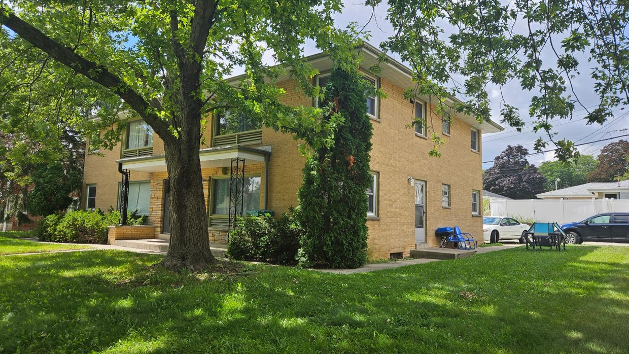 Two-story brick house with a large tree and green lawn.