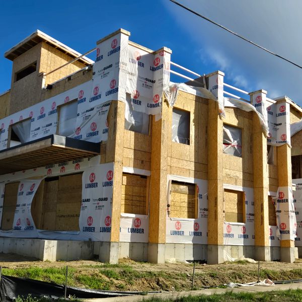 Partially constructed wooden house with lumber wrapping under a clear sky.