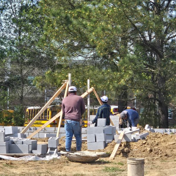 Three workers building a foundation with concrete blocks on a sunny day.