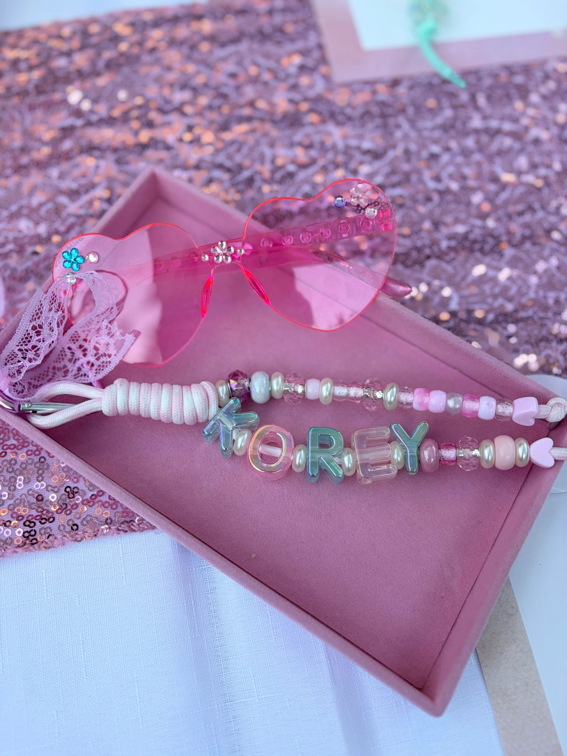 Pink heart-shaped glasses and a beaded bracelet with the name "KOREY" in a pink box.