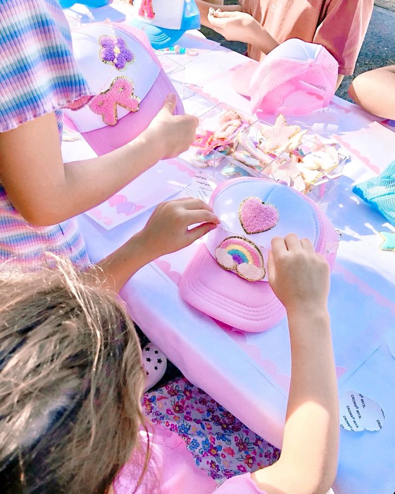 Children decorating pink hats with colourful patches at a sunny craft table. Sydney kids’ parties 