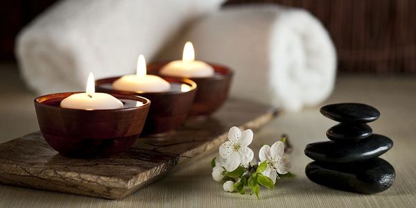 Image of 3 tealight candles, two white towels and a tower of flat black stones.