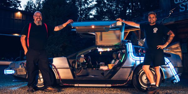 Side view of the DeLorean Time Machine with Chris and Ryan standing with their arms on the open door