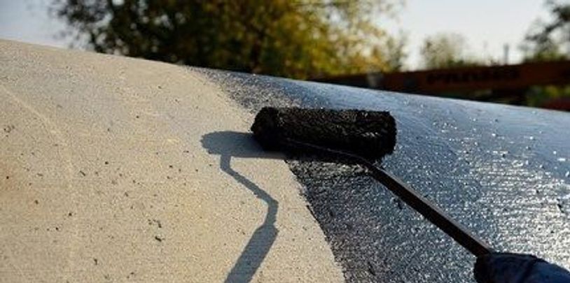 A paint roller applying black coating on a surface outdoors.