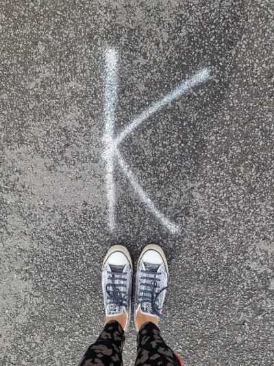 Shoes near a white letter K on asphalt.