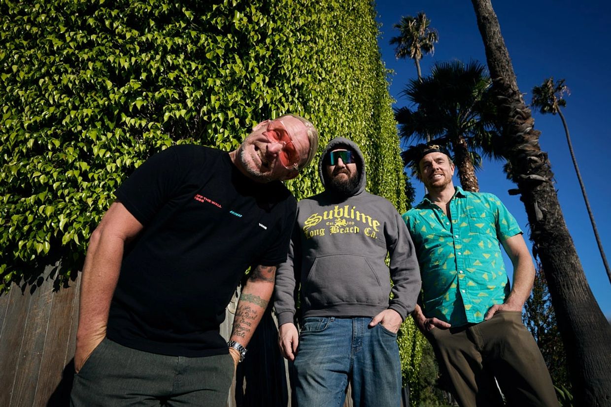 Three men posing outdoors near palm trees under a clear sky.
