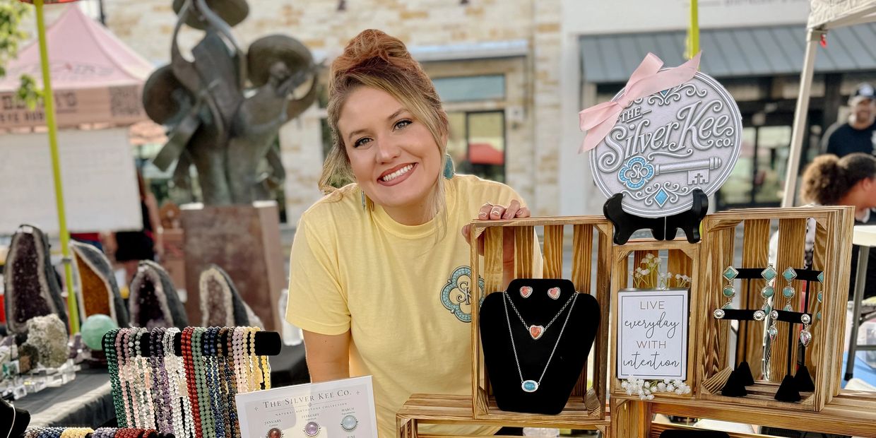 Woman smiling behind jewelry display at outdoor market.