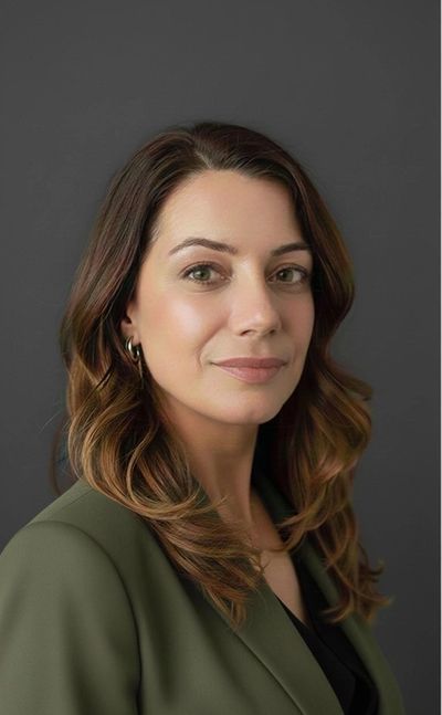 Professional portrait of a confident woman with wavy brown hair and green blazer.