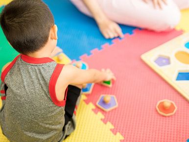 Young child playing with shape sorter puzzle on colorful foam mat.