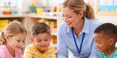 Teacher engaging with three young students in a classroom.