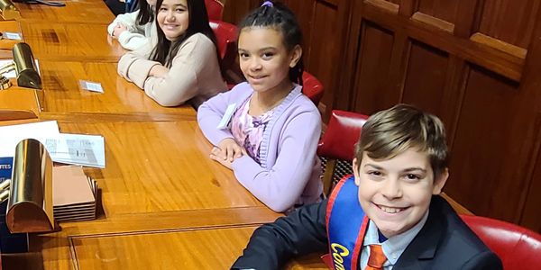 Three kids sitting at a wooden table smiling.