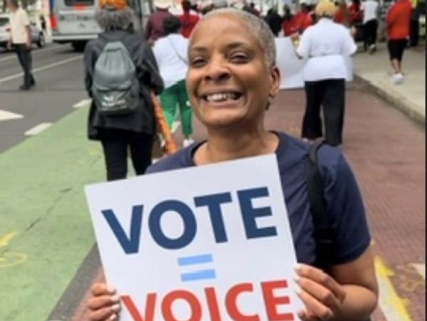 Woman smiling while holding a sign that says 'VOTE = VOICE'.