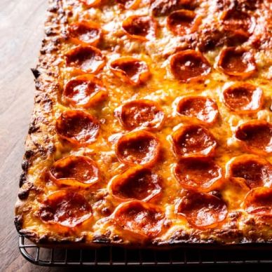 Square pepperoni pizza with crispy crust cooling on a rack.