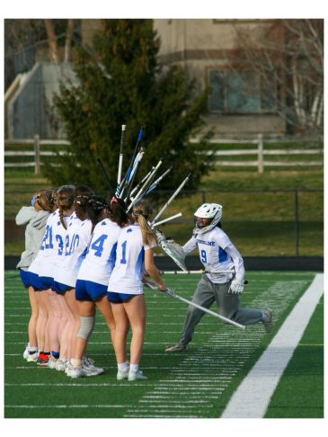 Girls lacrosse team with goalie celebrating on field.