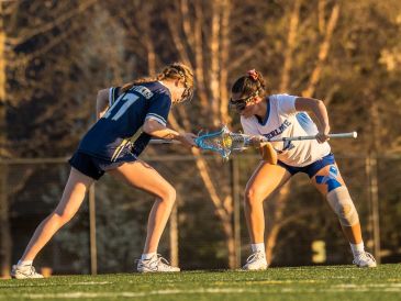 Two women playing lacrosse on a field.