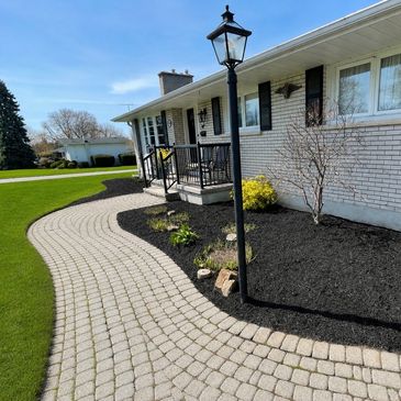 Curved brick walkway leading to a white house with a black lamp post and landscaped garden.