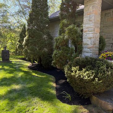 A landscaped garden with trimmed bushes and a stone pillar near a house.