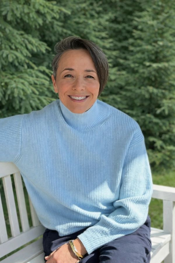 Smiling woman in blue sweater sitting on a white bench.